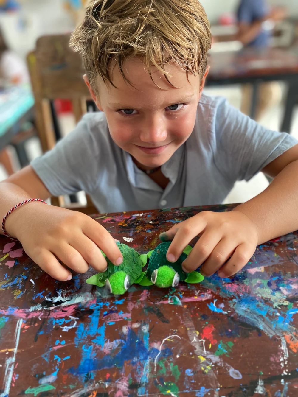 A boy is smiling mischeviously with two turtles that he has made