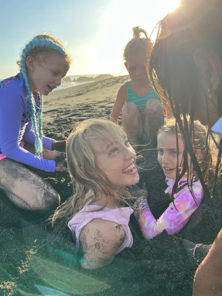 Five girls are on the beach burying each other in sand.