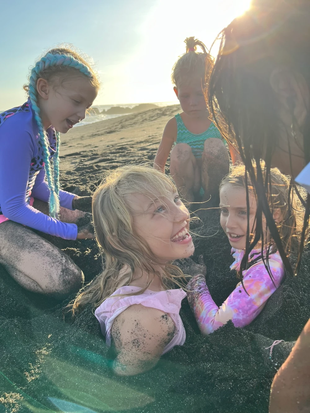 Five girls are on the beach burying each other in sand.