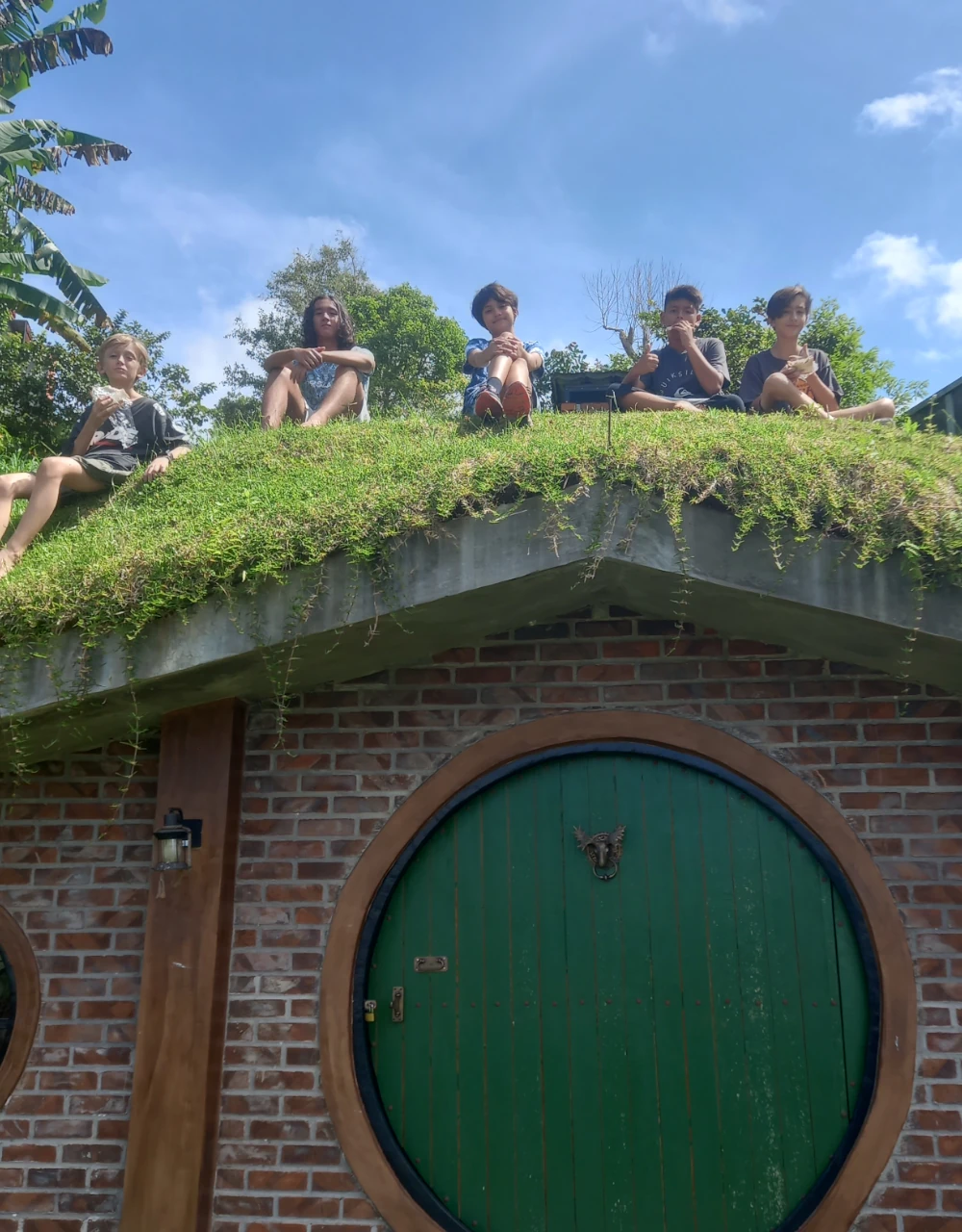Five boys sitting on a hobbit house grass roof above a big round door